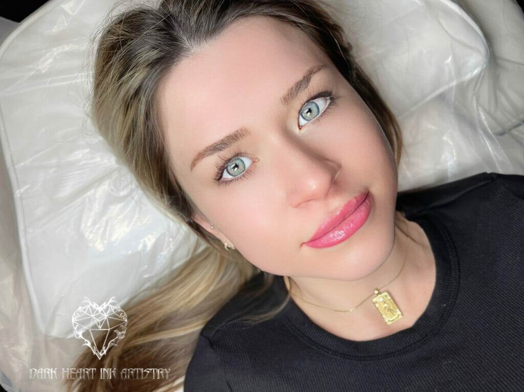 A woman with blue eyes receiving cosmetic tattooing while laying on a bed.