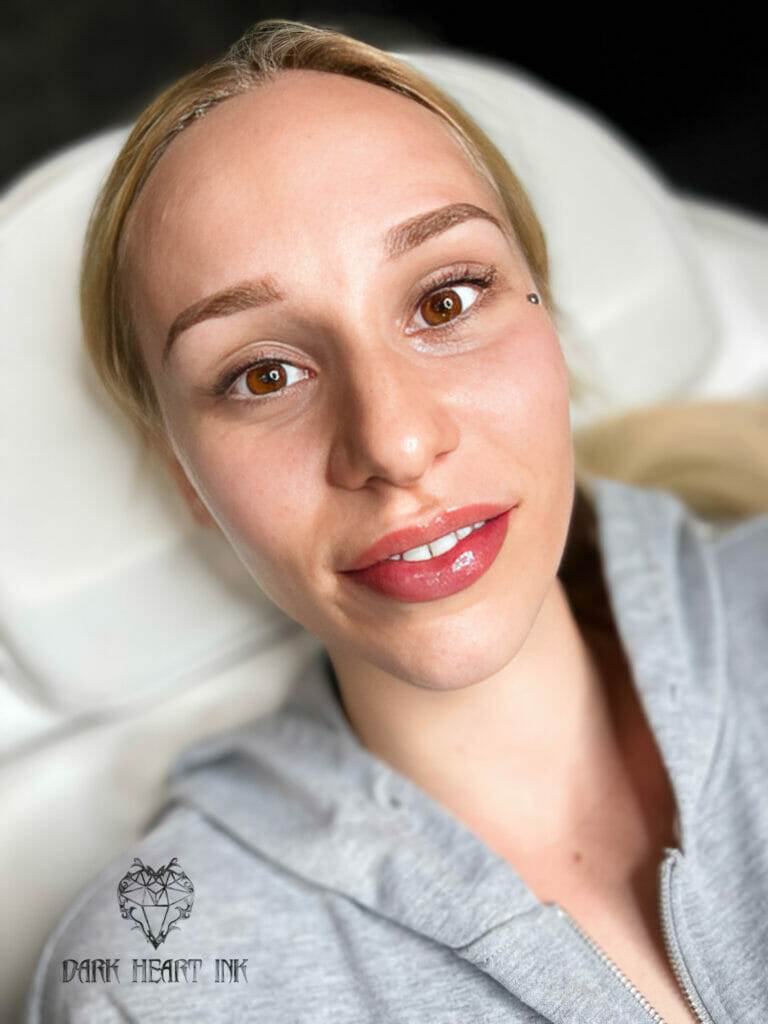 A woman with a smile on her face receiving cosmetic tattooing.