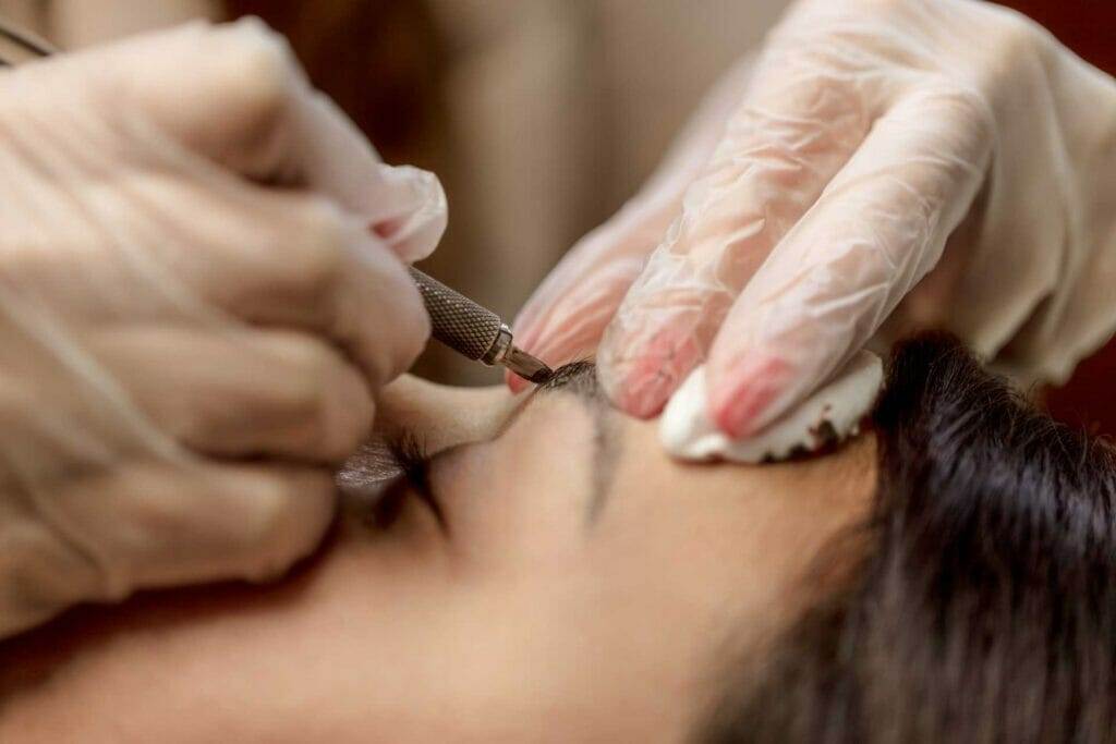 A woman getting her eyebrows waxed with microblading at a salon.