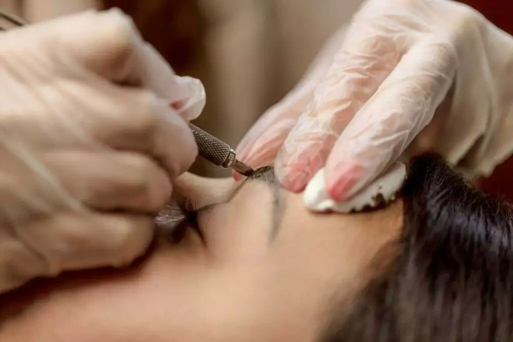 A woman getting her eyebrows waxed with microblading at a salon.