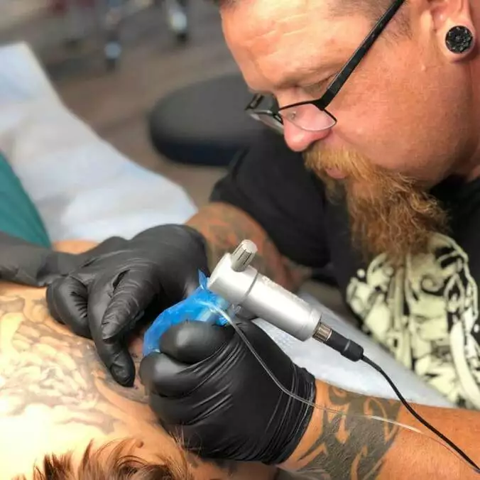 A tattoo artist is giving a home tattoo on a man's back.